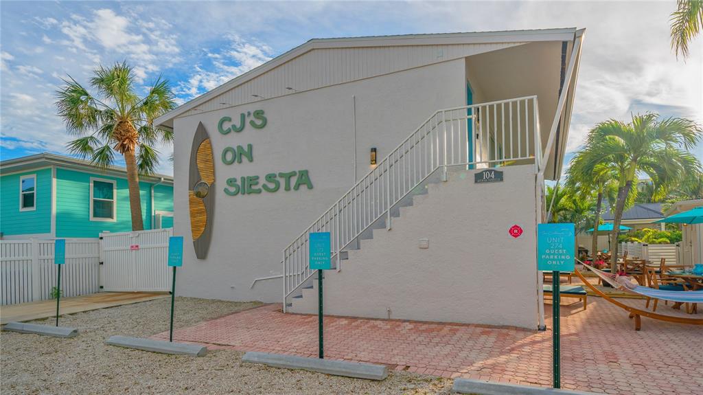 The exterior of a two-story building features a surfboard sign and guest parking spaces — 104 AVENIDA VENECCIA UNIT 171, SARASOTA, FL