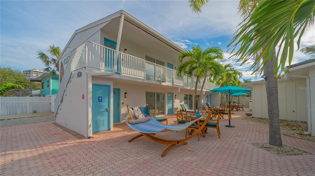 A two-story white building with blue doors, a hammock, and patio furniture on a brick courtyard — 104 AVENIDA VENECCIA UNIT 171, SARASOTA, FL
