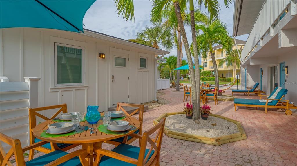 A patio area features a wooden dining set, lounge chairs, and palm trees on pavers — 104 AVENIDA VENECCIA UNIT 171, SARASOTA, FL