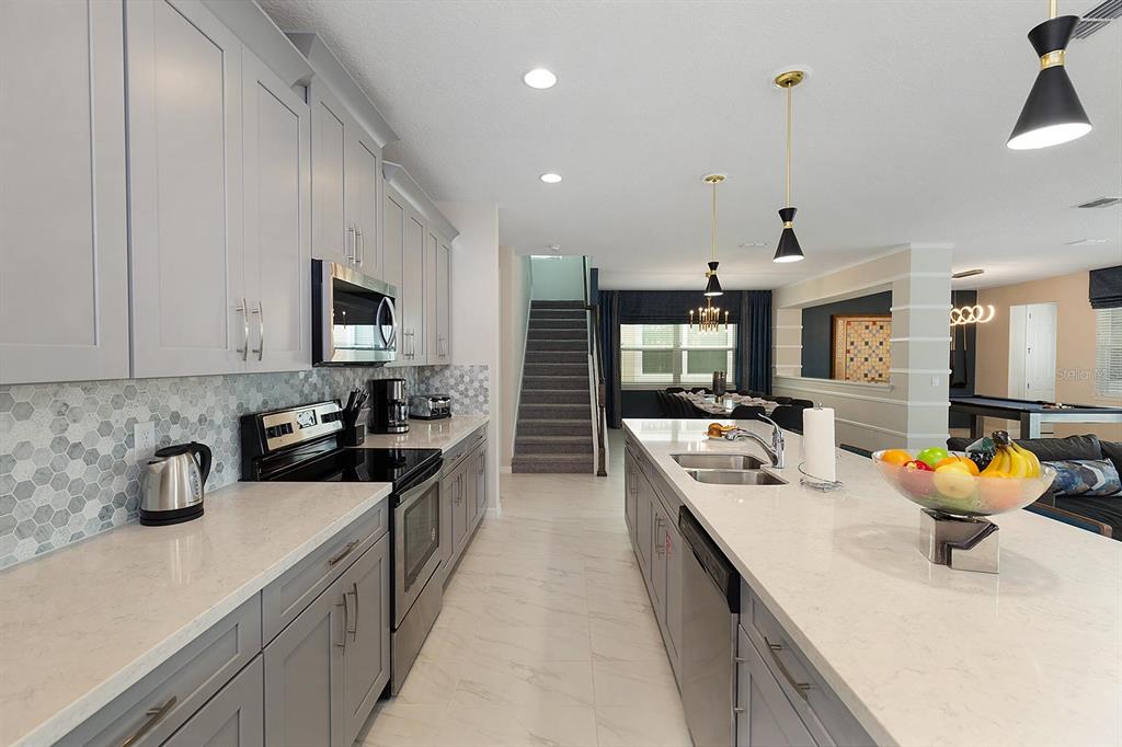 A modern kitchen features gray cabinets, white quartz countertops, and a central island — 1636 NASSAU POINT TRAIL, KISSIMMEE, FL