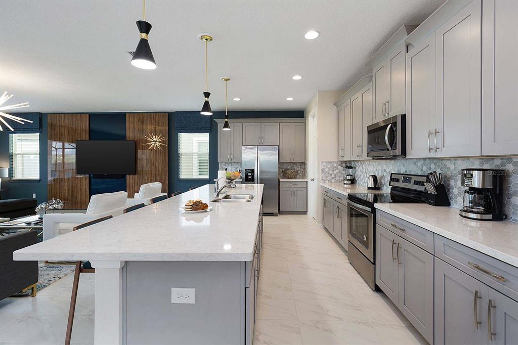A modern kitchen features gray cabinets, white quartz countertops, and a large central island — 1636 NASSAU POINT TRAIL, KISSIMMEE, FL