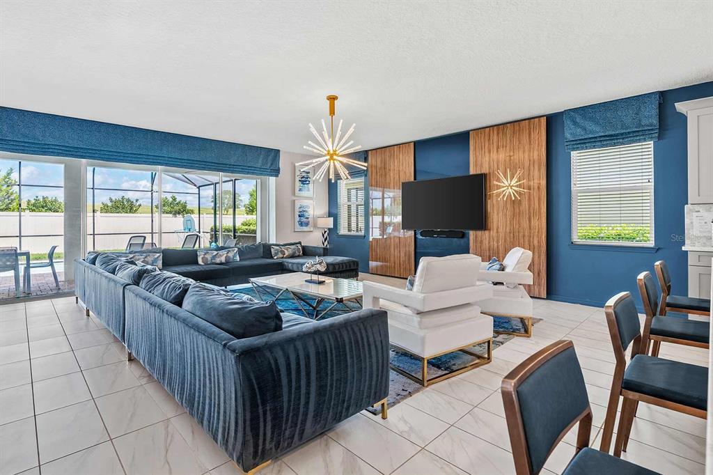 A living room features a large blue sectional, white armchairs, and a wood-paneled media wall — 1636 NASSAU POINT TRAIL, KISSIMMEE, FL