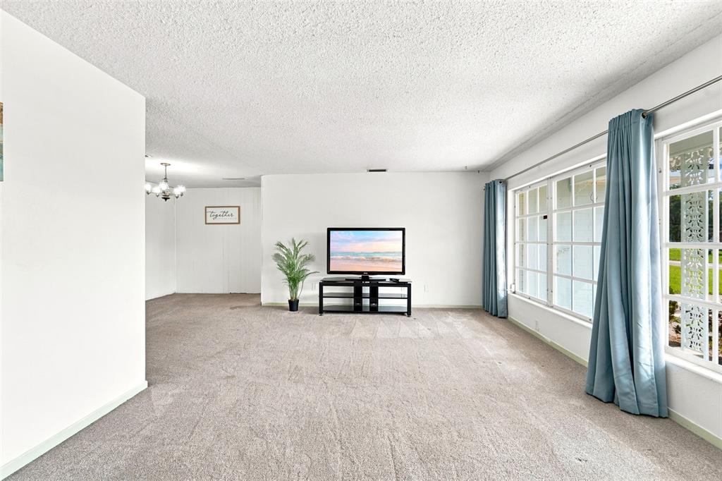 A living room with beige carpet, white walls, a television on a stand, and windows — 790 S BOUNDARY AVENUE, DELAND, FL
