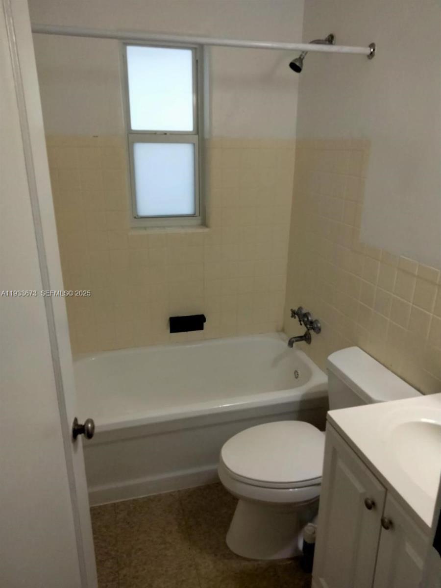 A bathroom features a white bathtub, a toilet, a vanity, and beige wall tiles — 6950 Byron Ave # 4, Miami Beach FL 33141, MIAMI BEACH, FL
