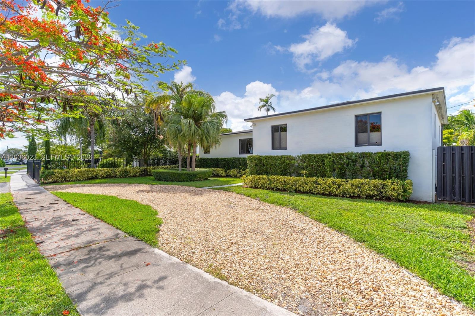 A white house with a gravel driveway and manicured hedges sits under a blue sky — 8281 SW 27th Ln, Miami FL 33155, MIAMI, FL