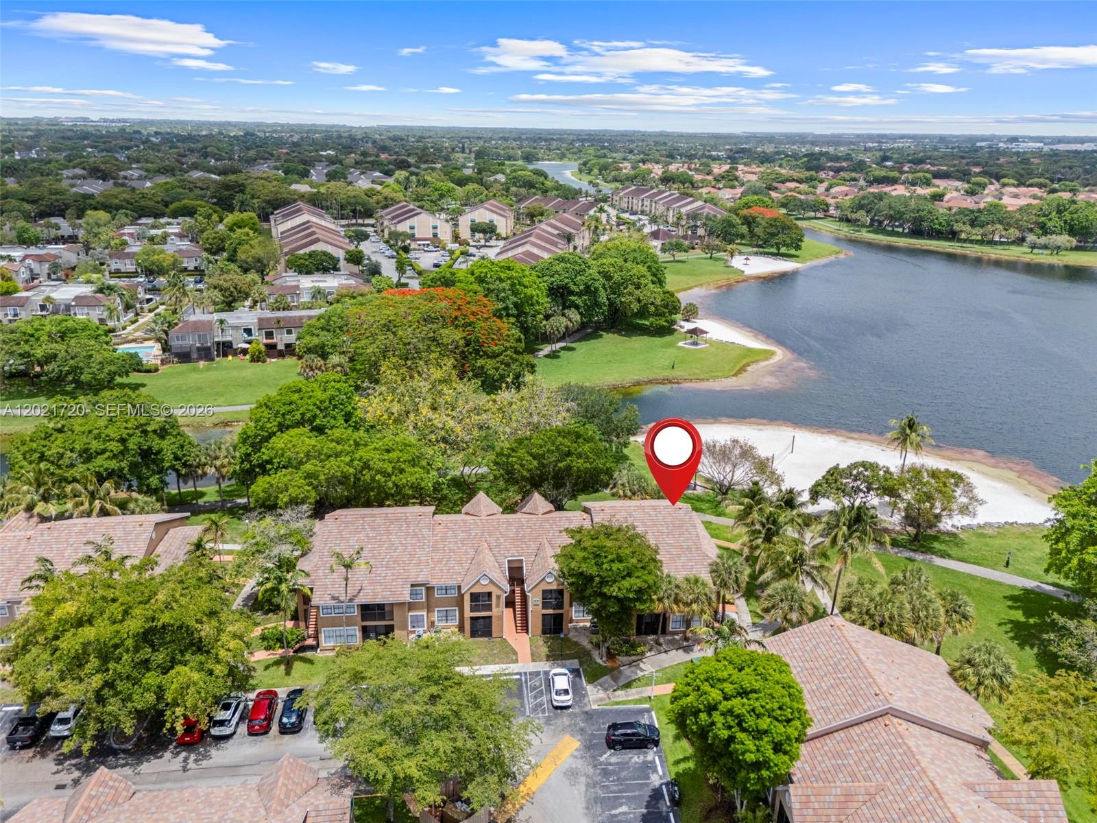 An aerial view shows a multi-story apartment building situated near a lake and sandy beach — MIAMI, FL