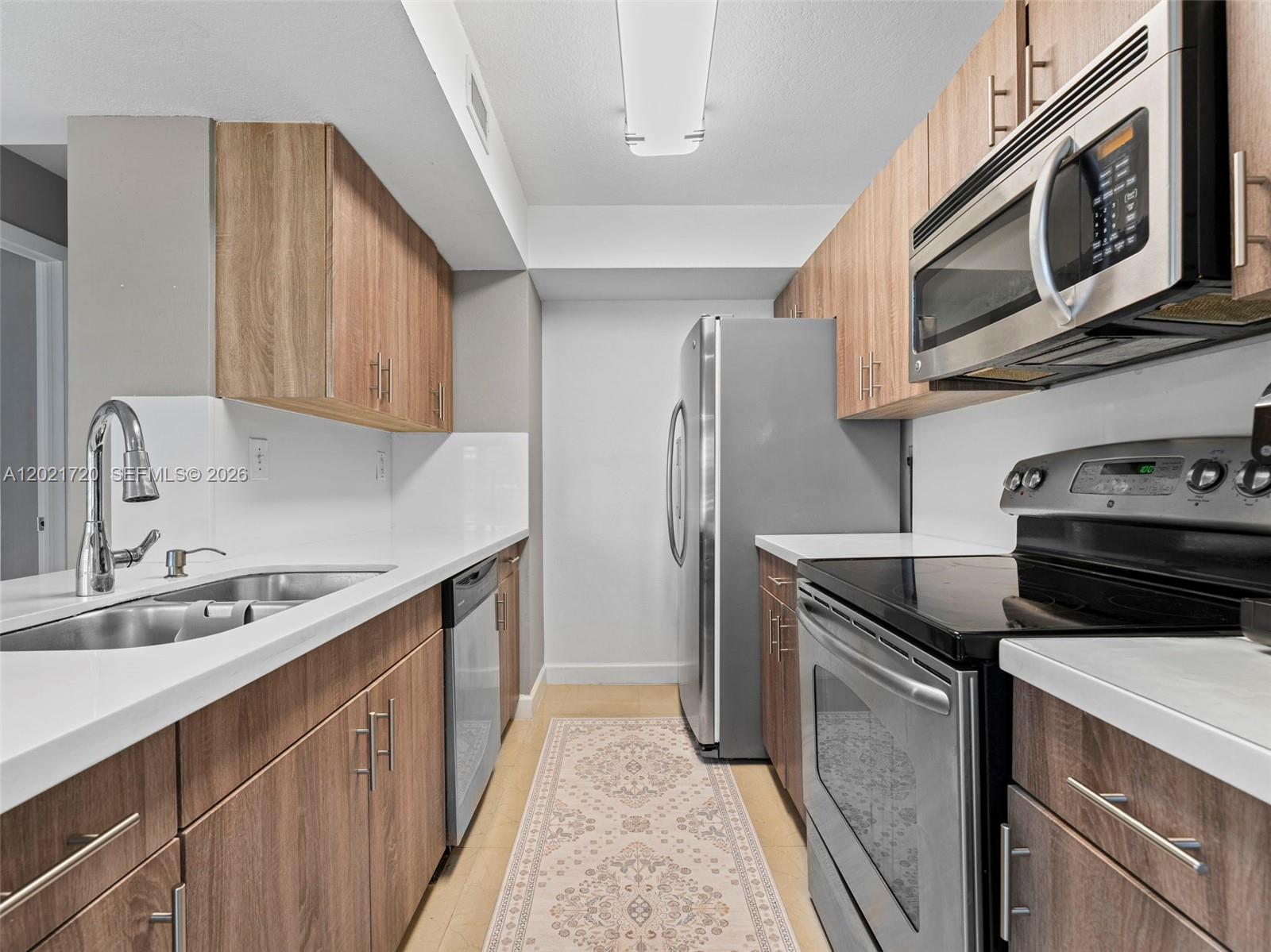 A galley kitchen features wood-tone cabinets, stainless steel appliances, and white countertops — MIAMI, FL