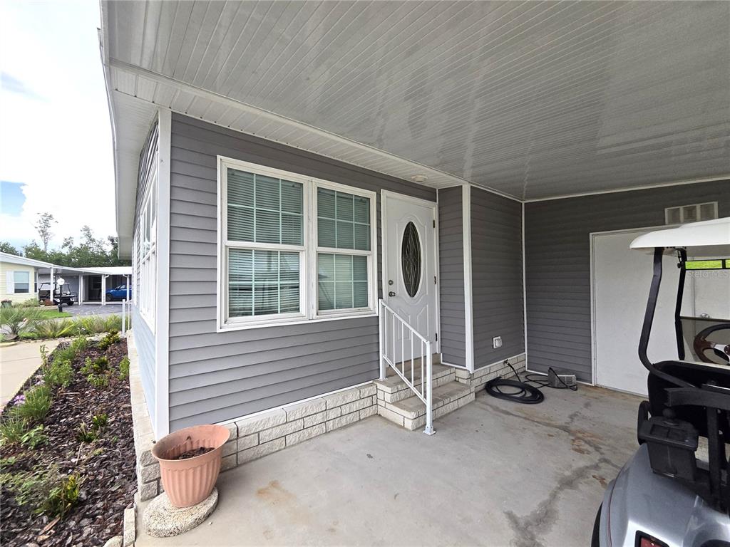 A gray-sided house exterior features a covered concrete porch, a white front door, and steps — 332 VICTORIA DRIVE, HAINES CITY, FL