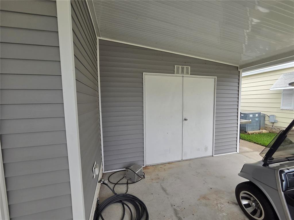 A gray-sided storage shed with double white doors sits under a covered carport — 332 VICTORIA DRIVE, HAINES CITY, FL