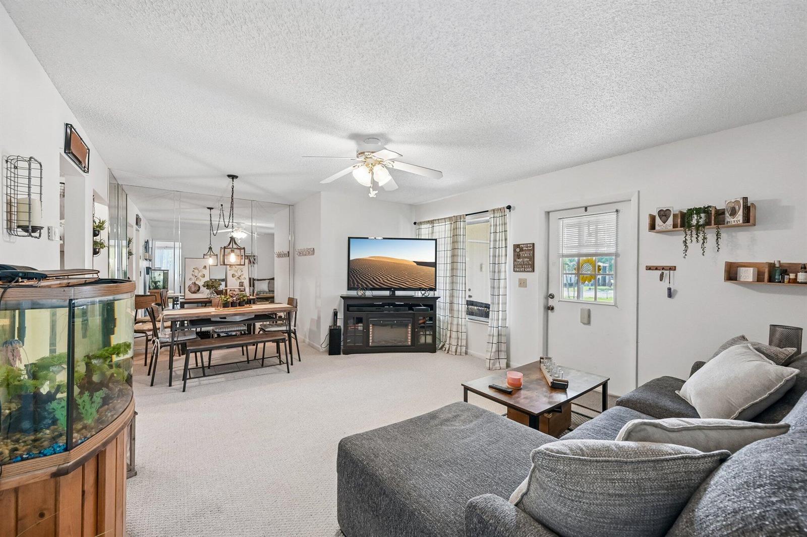 A living room with carpeted floors, a sectional sofa, a television, and an adjacent dining area — 5901 Whispering Pine Way # 2, FL 33463, FL
