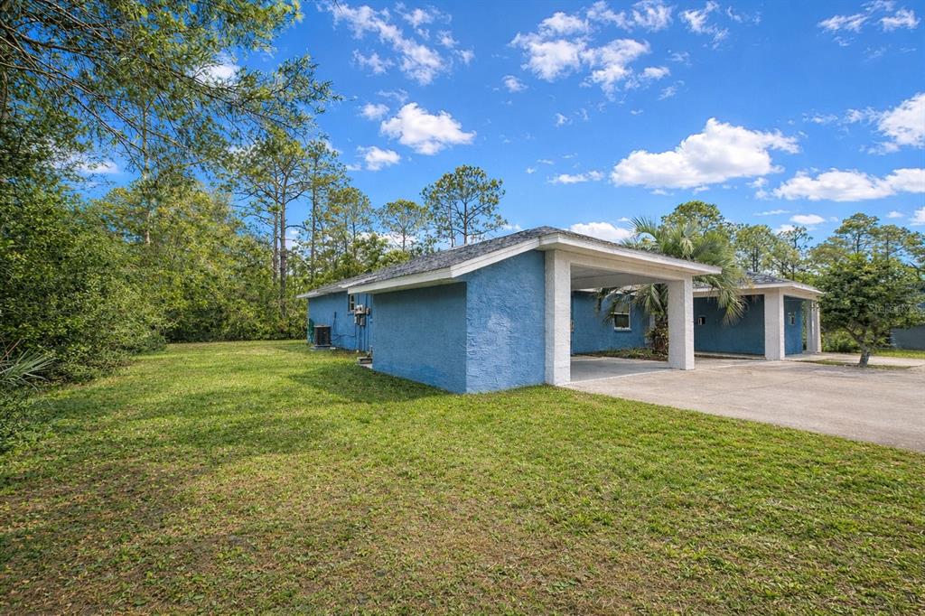 A blue house with a concrete carport sits on a grassy lot with surrounding trees — 9 WHEELER PLACE UNIT A, B, PALM COAST, FL