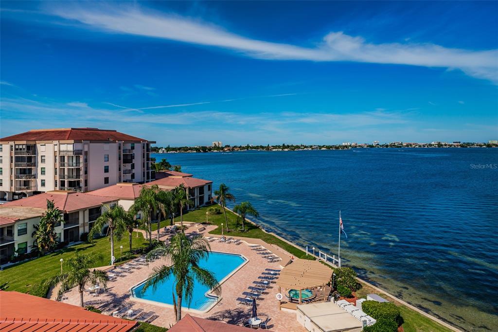 An aerial view shows a swimming pool and patio area next to a waterfront apartment complex — 6051 SUN BOULEVARD UNIT 305, ST PETERSBURG, FL