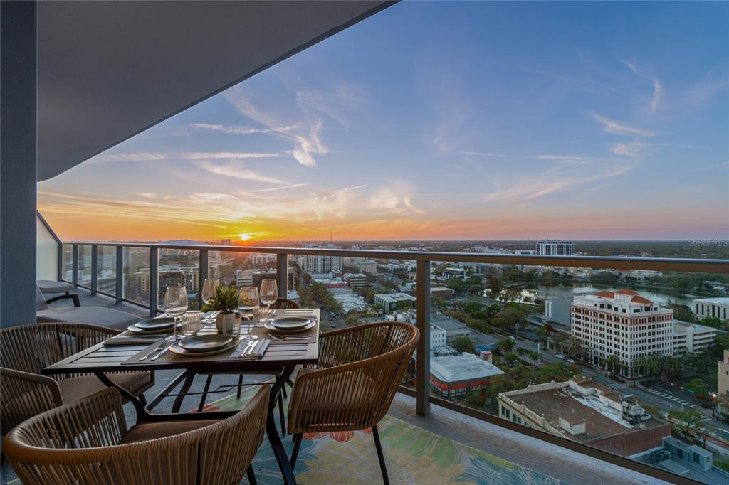 A high-rise balcony features a dining set overlooking a city skyline at sunset — 400 CENTRAL AVENUE UNIT 2102, ST PETERSBURG, FL