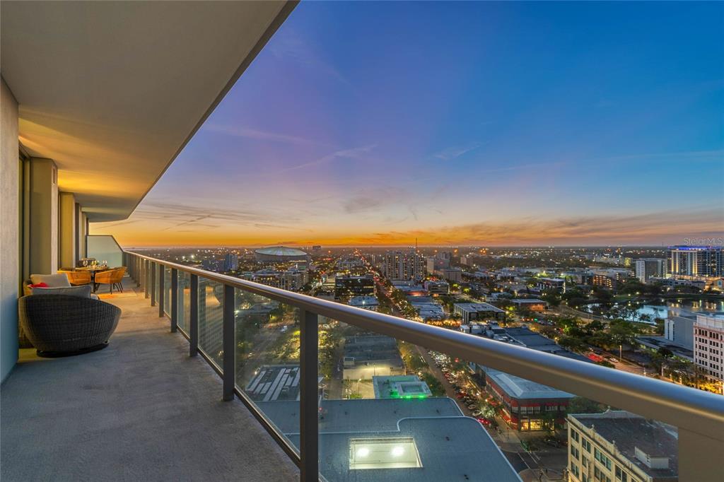 A high-rise balcony with outdoor seating overlooks a city skyline at sunset — 400 CENTRAL AVENUE UNIT 2102, ST PETERSBURG, FL