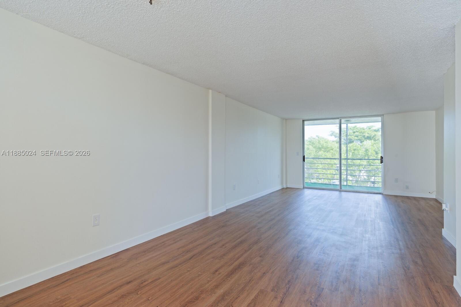 An empty living room features wood-look flooring, white walls, a textured ceiling, and sliding glass doors — 14180 SW 84th St # G, Miami FL 33183, MIAMI, FL