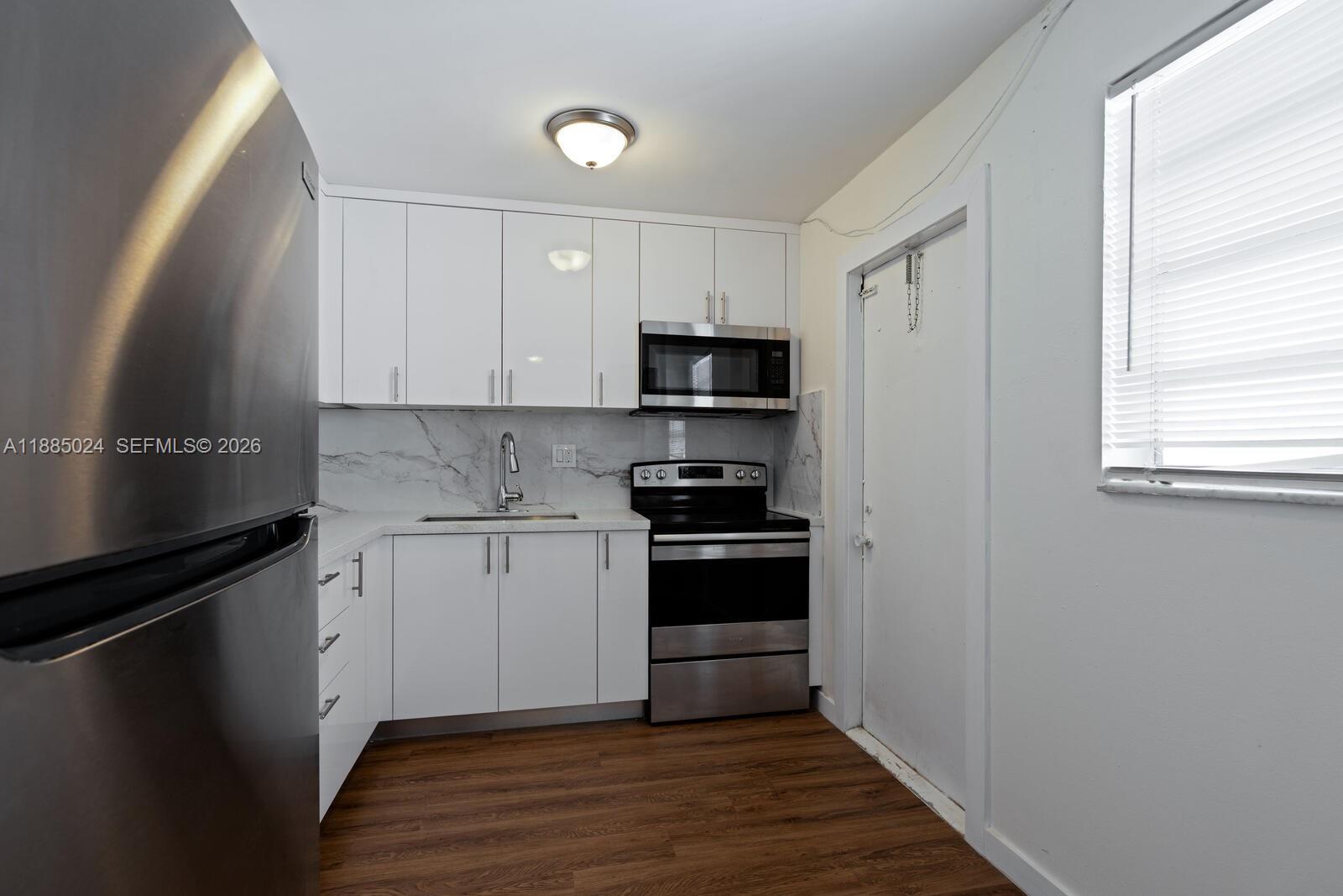 A kitchen features white cabinets, stainless steel appliances, marble-look backsplash, and wood-style flooring — 14180 SW 84th St # G, Miami FL 33183, MIAMI, FL