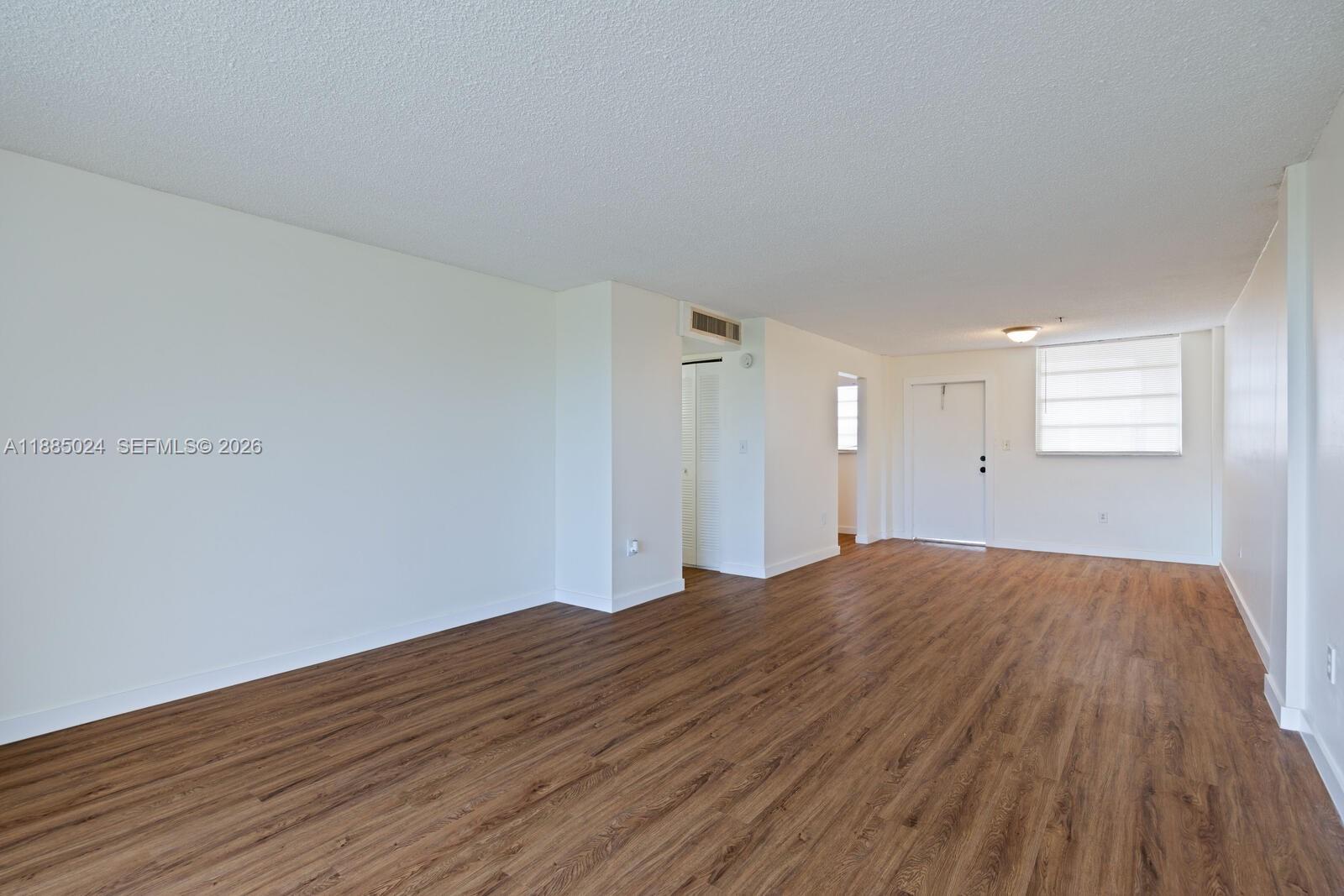 An empty room features white walls, wood-look flooring, and a white entry door — 14180 SW 84th St # G, Miami FL 33183, MIAMI, FL
