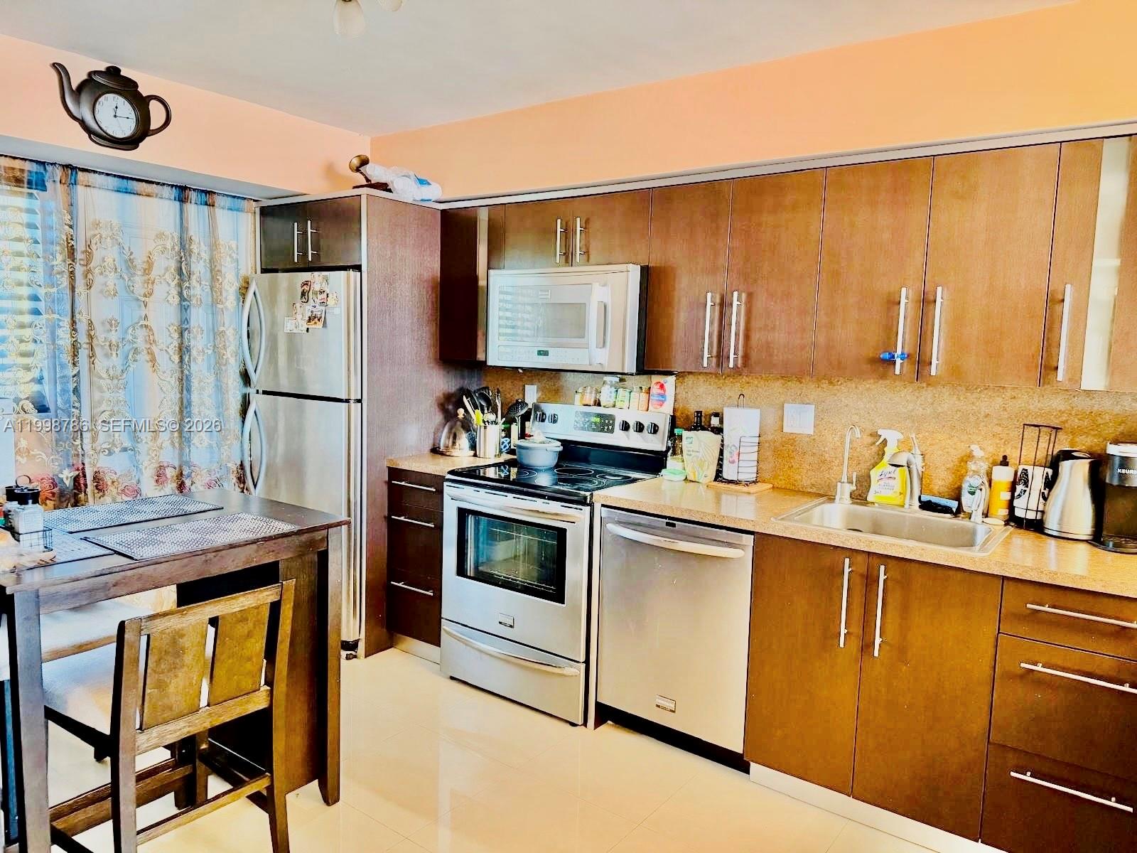 A kitchen features wood cabinets, stainless steel appliances, and a small dining table — 1150 NE 191st St # 38, Miami FL 33179, MIAMI, FL