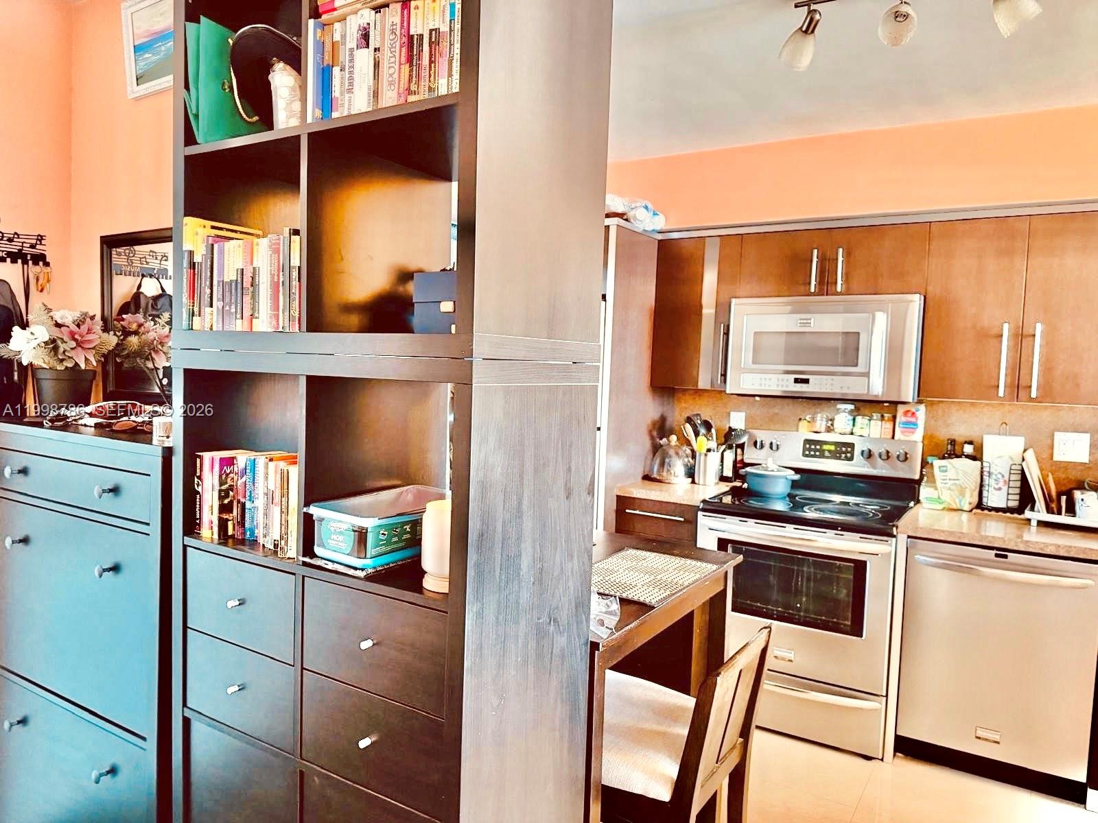 A kitchen with wooden cabinets and stainless steel appliances sits beside a dark shelving unit — 1150 NE 191st St # 38, Miami FL 33179, MIAMI, FL