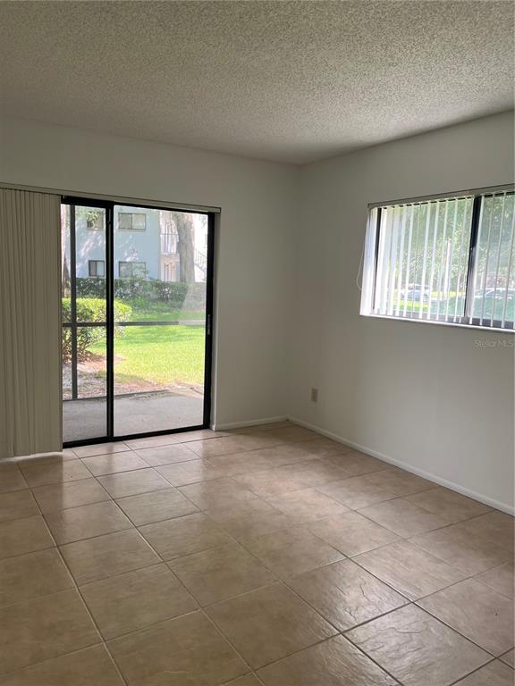 An empty room features beige tile flooring, a sliding glass door, and a window — 3300 FOX CHASE CIRCLE N UNIT 226, PALM HARBOR, FL