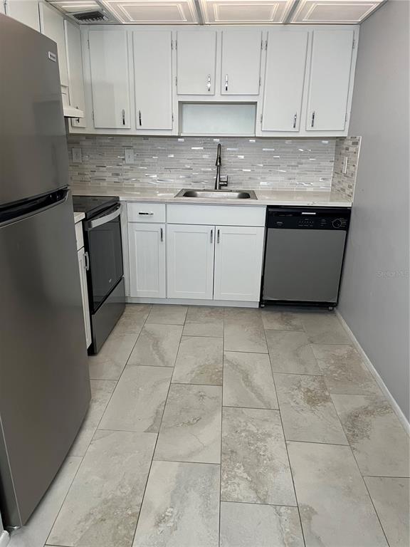 A kitchen features white cabinets, stainless steel appliances, a tiled backsplash, and light-colored floor tiles — 3300 FOX CHASE CIRCLE N UNIT 226, PALM HARBOR, FL