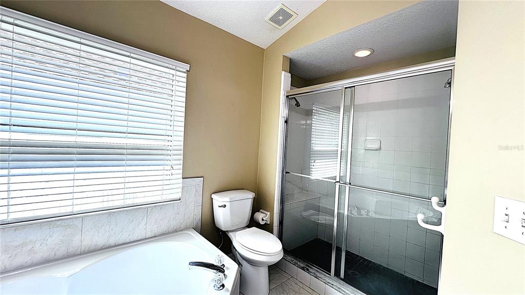 A bathroom features a soaking tub, a toilet, and a glass-enclosed shower with white tiles — 10903 RUSHWOOD WAY, CLERMONT, FL