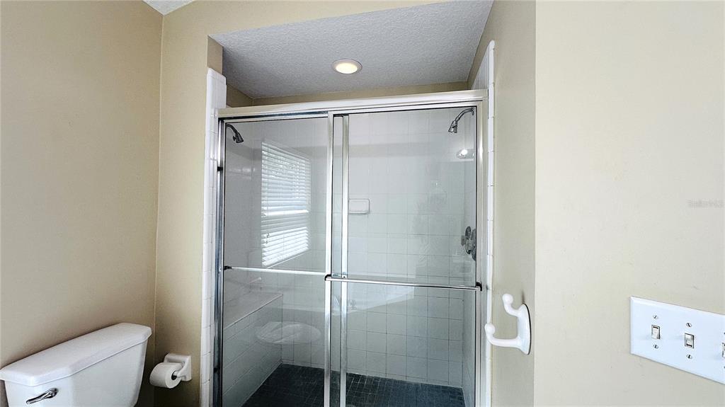 A bathroom features a glass-enclosed shower, a toilet, and a light switch on the wall — 10903 RUSHWOOD WAY, CLERMONT, FL