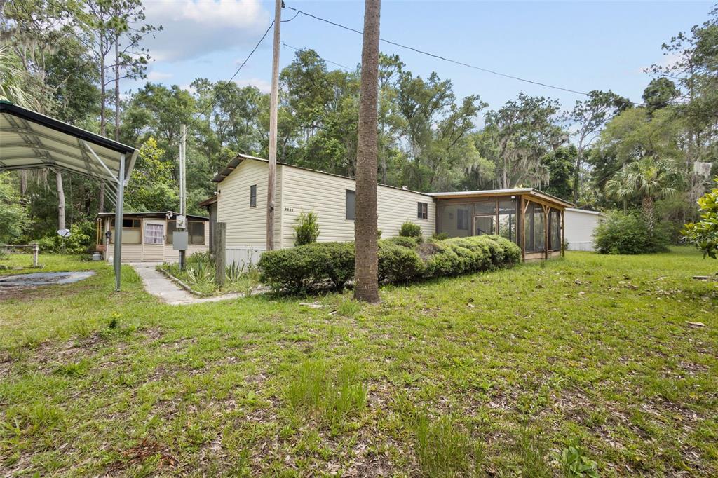 A single-story mobile home with a screened-in porch sits on a grassy, wooded lot — 9949 NW 55TH STREET, CHIEFLAND, FL