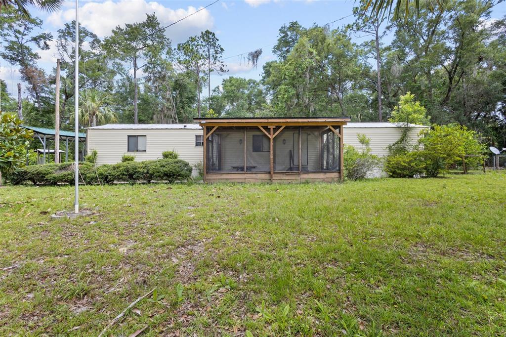 A single-story mobile home features a wooden screened-in porch and is surrounded by trees — 9949 NW 55TH STREET, CHIEFLAND, FL