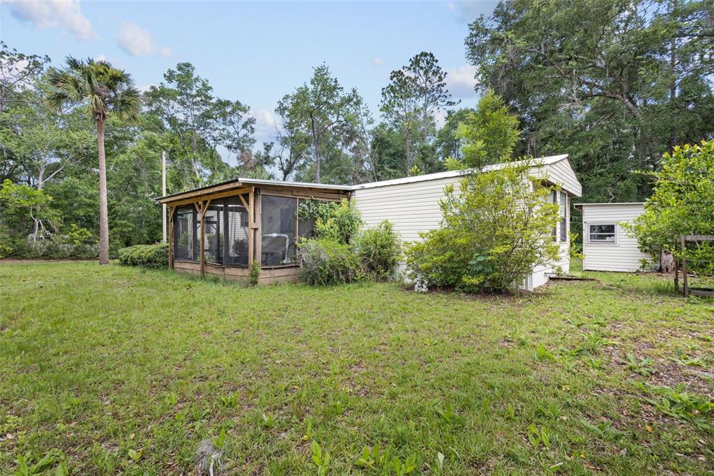 A mobile home with a screened-in porch sits on a grassy lot surrounded by trees — 9949 NW 55TH STREET, CHIEFLAND, FL