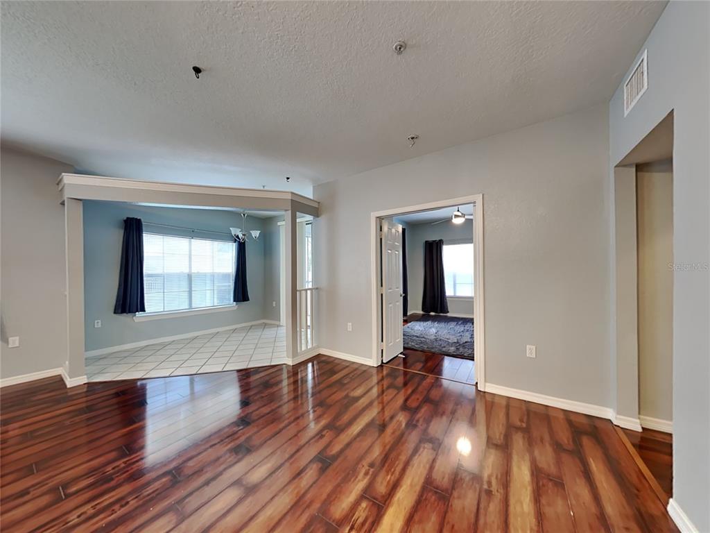 A living room with dark wood flooring leads to a tiled dining area and bedroom — 2328 MIDTOWN TERRACE UNIT 1024, ORLANDO, FL