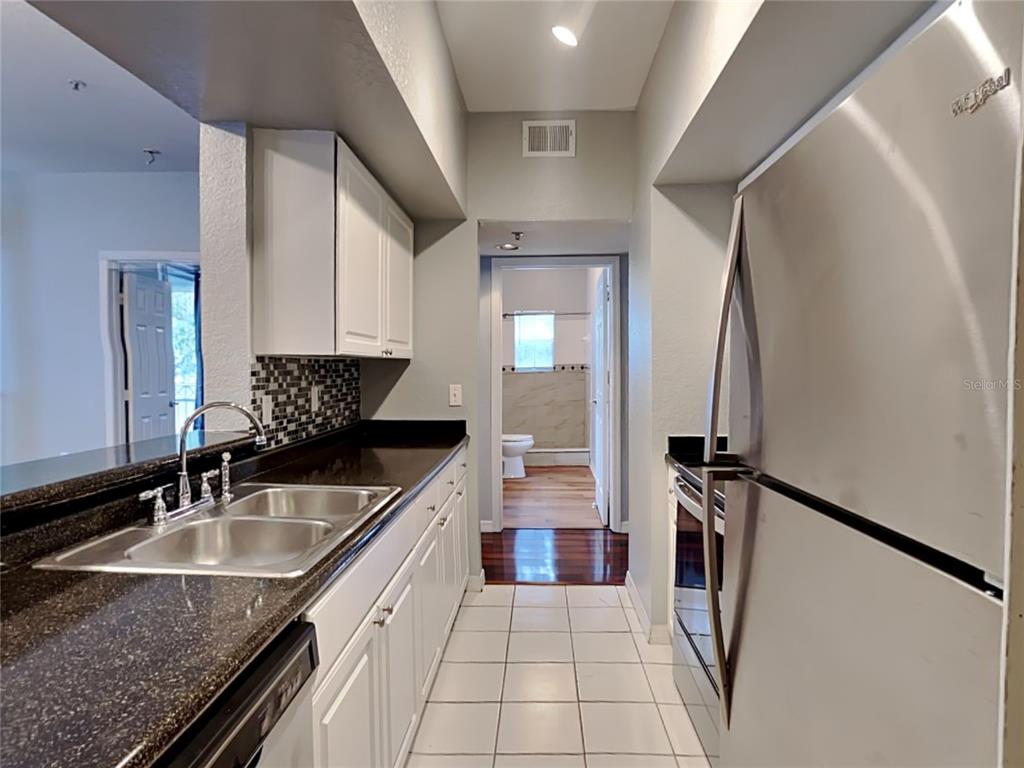 A galley kitchen features white cabinets, dark countertops, stainless steel appliances, and tiled flooring — 2328 MIDTOWN TERRACE UNIT 1024, ORLANDO, FL