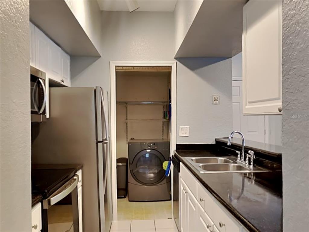 A kitchen with dark countertops and stainless steel appliances leads to a laundry closet — 2328 MIDTOWN TERRACE UNIT 1024, ORLANDO, FL