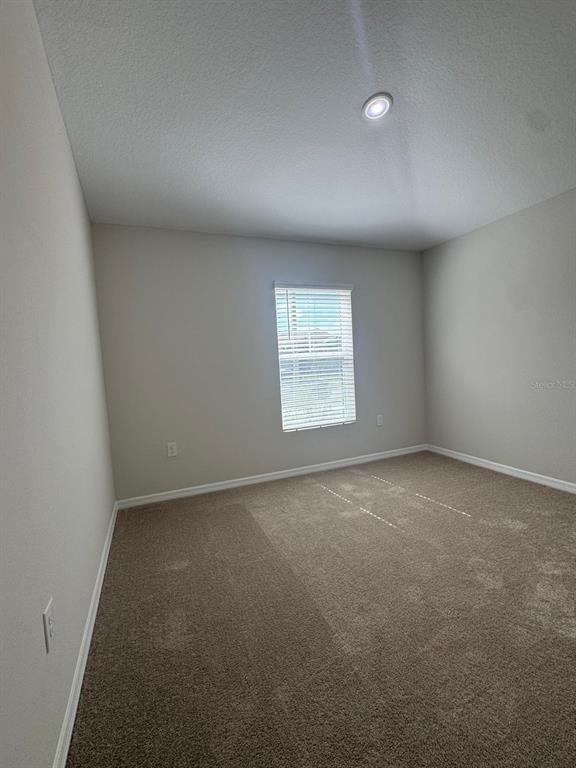 An empty bedroom features beige walls, brown carpeting, a single window with blinds, and recessed lighting — 1049 FORESHORE LANE, HAINES CITY, FL
