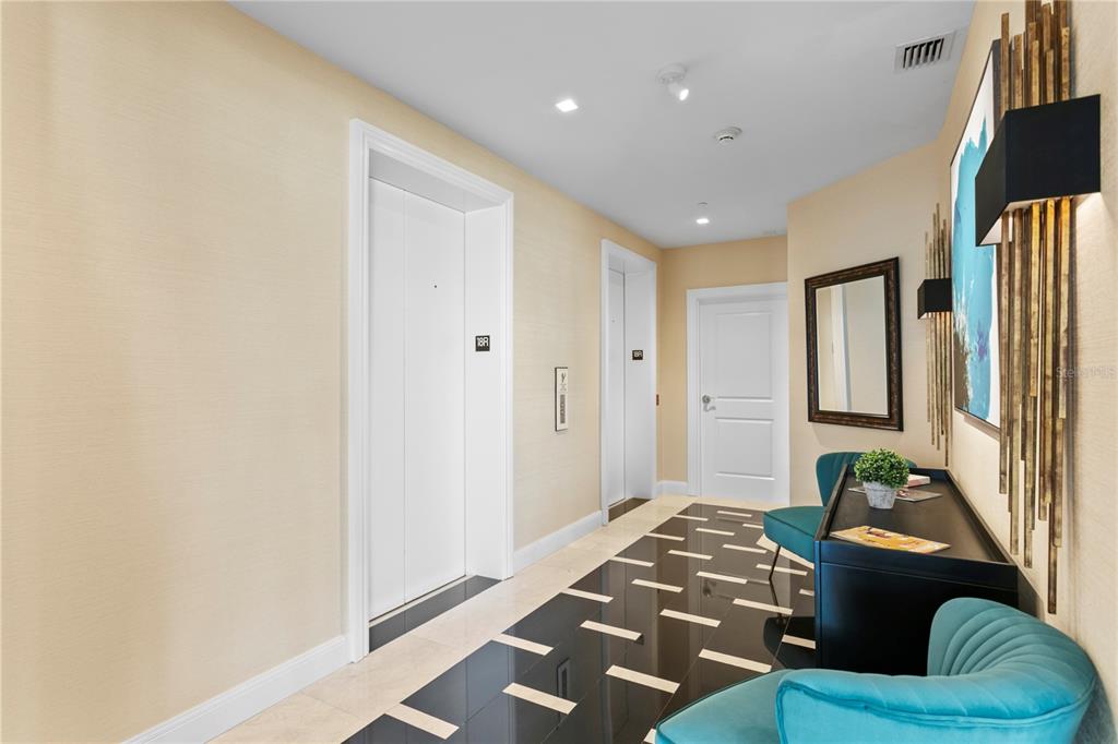 A hallway features two white elevator doors, a black console table, and teal velvet chairs — 450 KNIGHTS RUN AVENUE UNIT 1801, TAMPA, FL