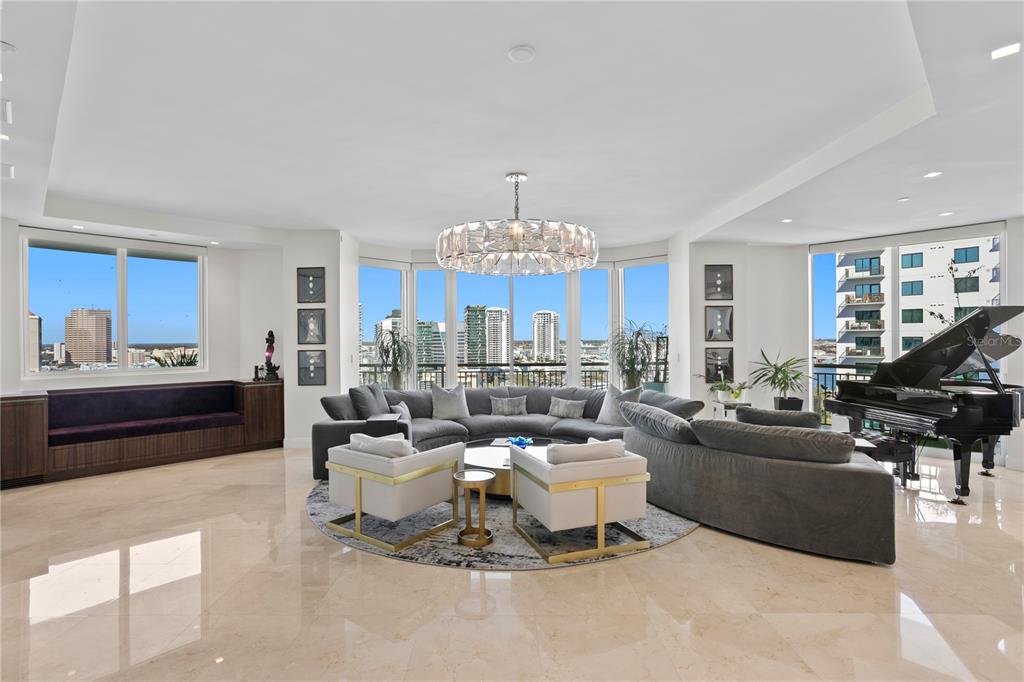 A spacious living room features a large sectional sofa, a grand piano, and floor-to-ceiling windows — 450 KNIGHTS RUN AVENUE UNIT 1801, TAMPA, FL