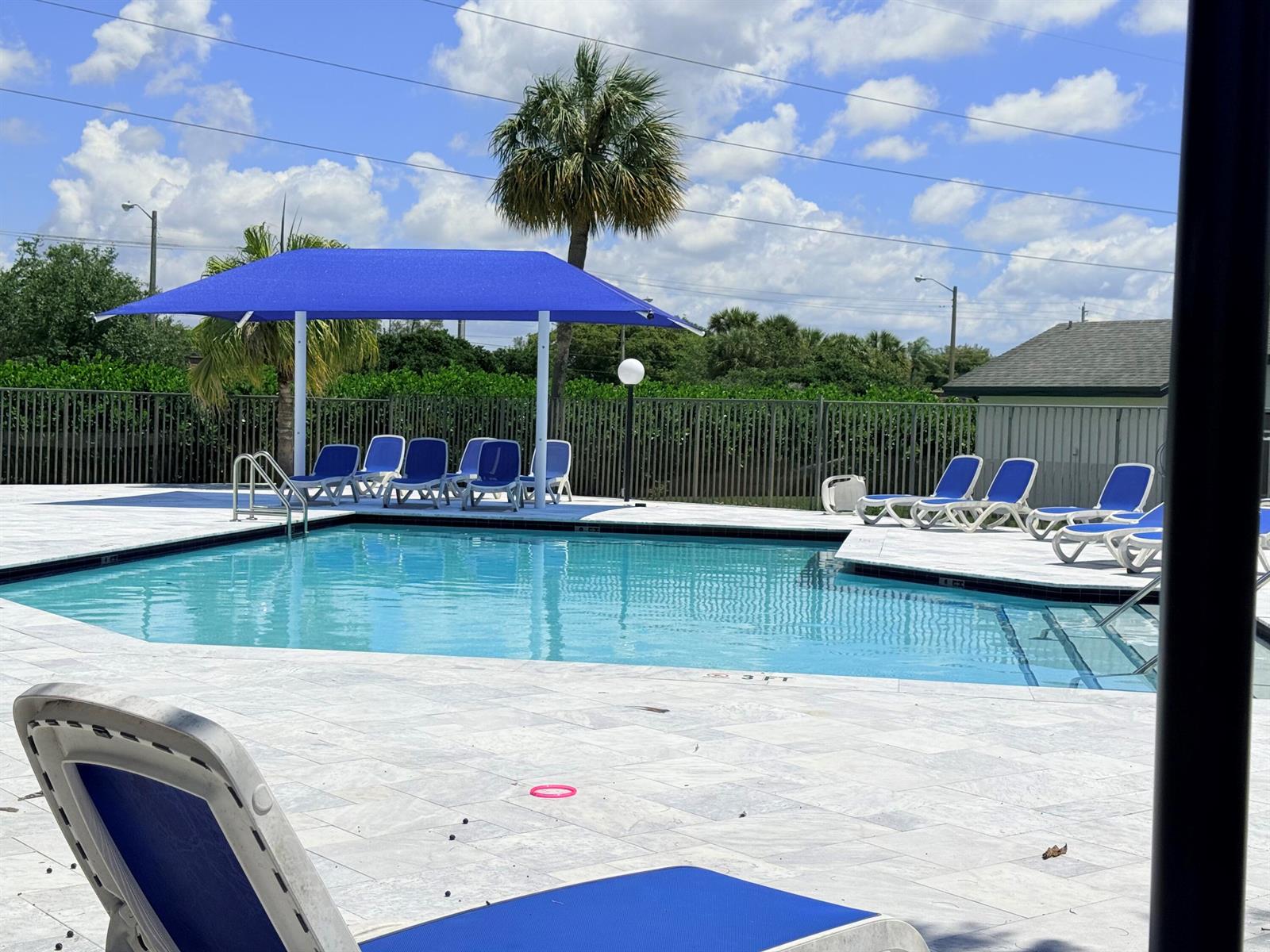 An outdoor swimming pool with blue lounge chairs and a shade structure on a patio — 7797 San Marcos Place, Boca Raton FL 33433, BOCA RATON, FL