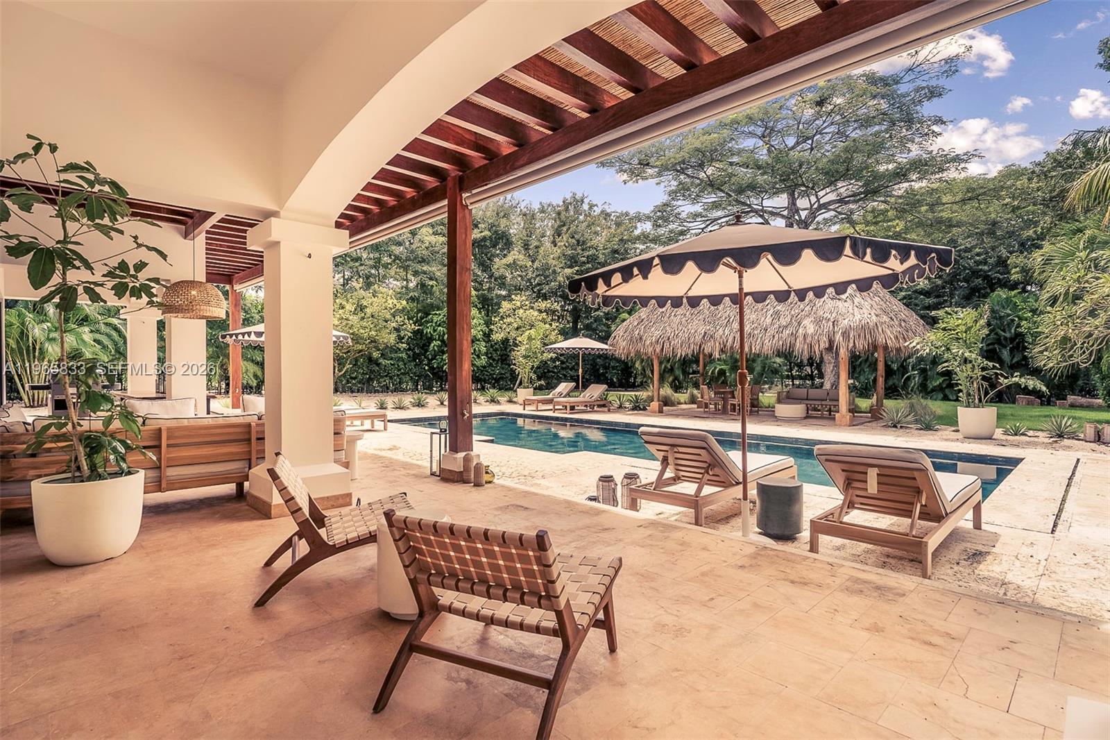 A covered patio overlooks a swimming pool, lounge chairs, and a thatched-roof gazebo — 90 Reserva De Golf, IA 50319, IA
