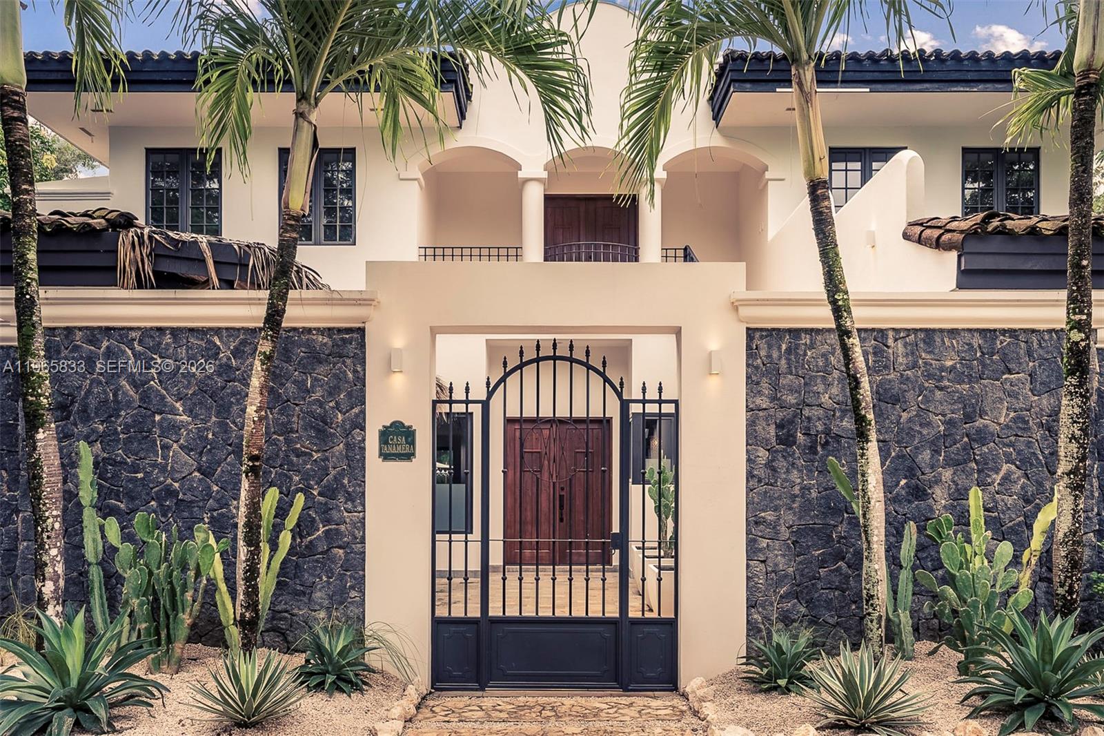 The exterior of a two-story house features a stone wall, palm trees, and iron gate — 90 Reserva De Golf, IA 50319, IA