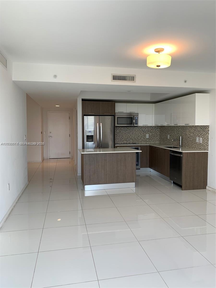 A modern kitchen features dark wood lower cabinets, white upper cabinets, and white tile flooring — 5252 NW 85th Ave # 1104, Doral FL 33166, DORAL, FL