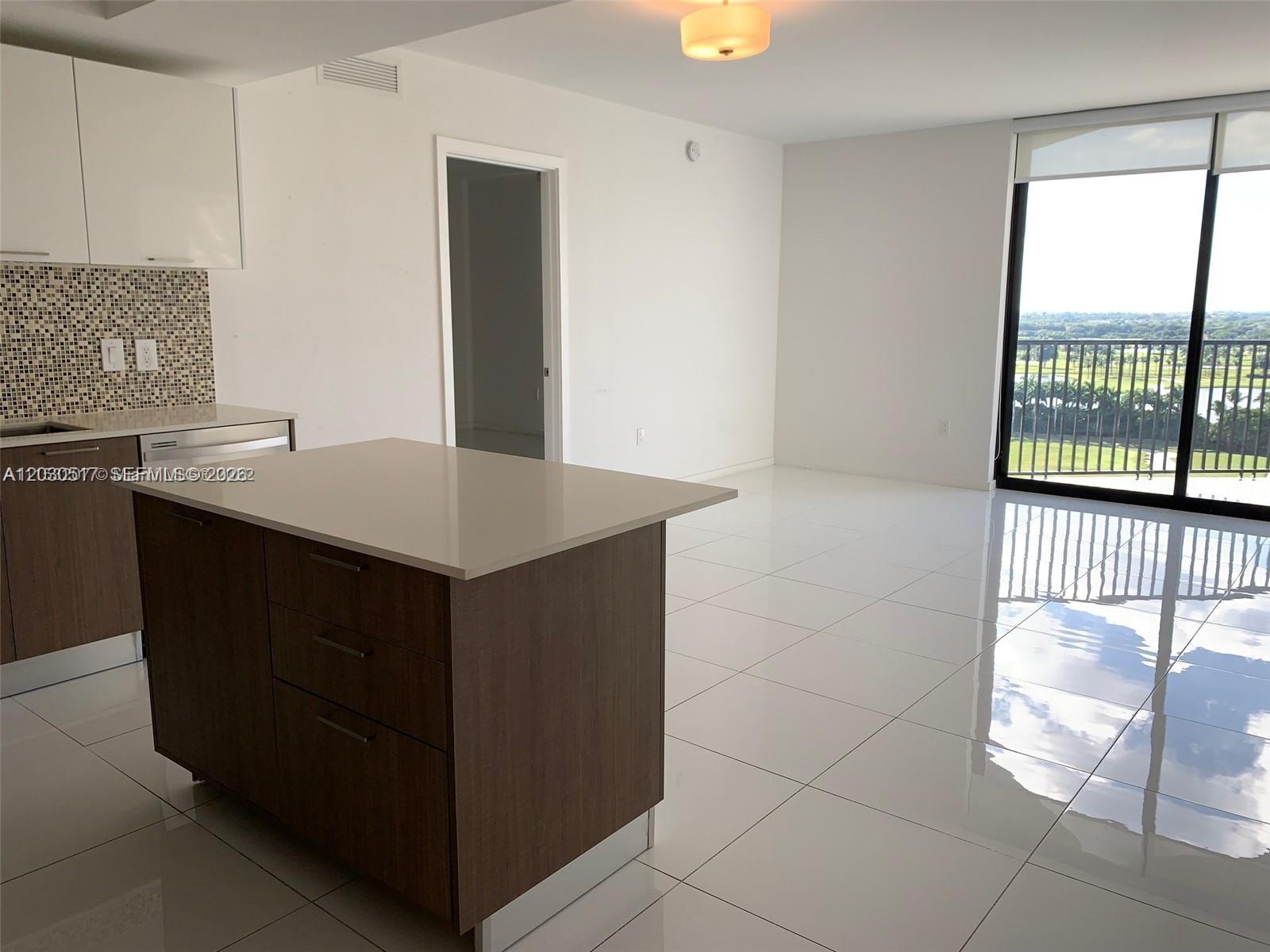 A modern kitchen with a center island and white tile floors overlooks a balcony view — 5252 NW 85th Ave # 1104, Doral FL 33166, DORAL, FL