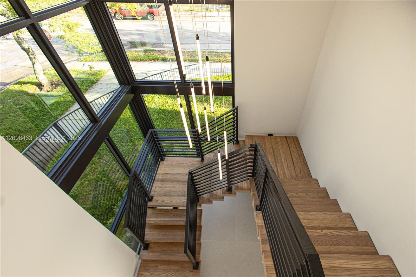 A wooden staircase with black railings is illuminated by modern pendant lights near large windows — 5800 NW 5th Ave #5800, Miami FL 33127, MIAMI, FL