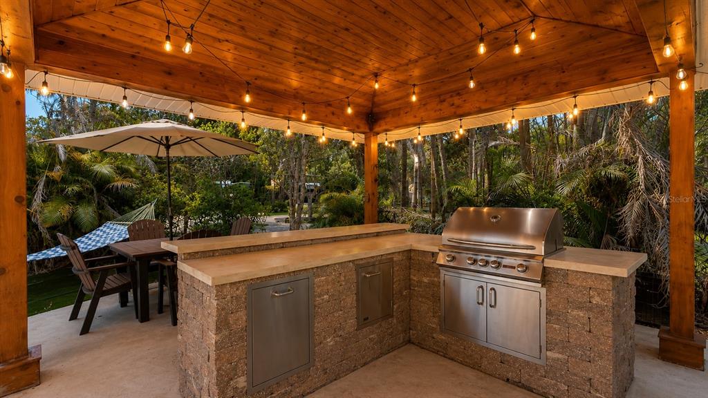 An outdoor kitchen with a stainless steel grill and stone base sits under a wooden pergola — 264 SADDLE LANE, RIVER RANCH, FL