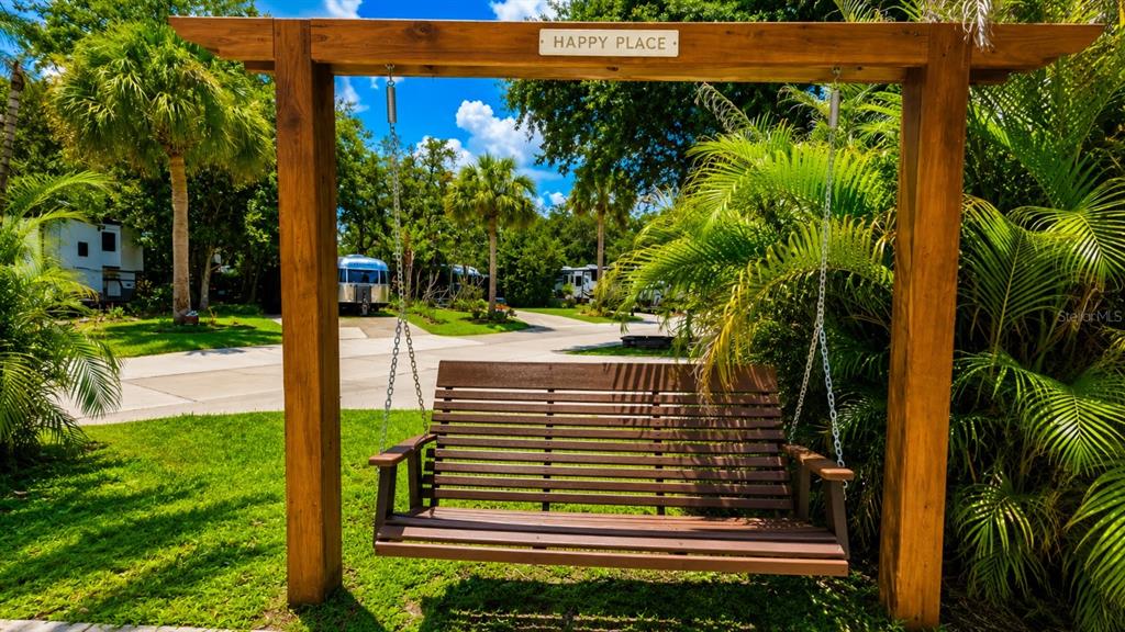 A wooden porch swing hangs from a pergola frame in a landscaped outdoor area — 264 SADDLE LANE, RIVER RANCH, FL
