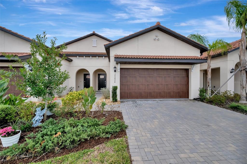 A single-story house with a brown garage door, arched entryway, and a paved driveway — 17436 HOLLY WELL AVENUE, WIMAUMA, FL
