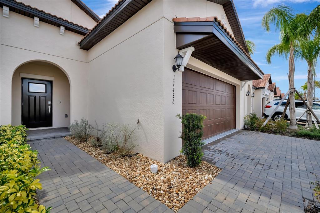 A beige house exterior features a dark brown garage door, a front door, and pavers — 17436 HOLLY WELL AVENUE, WIMAUMA, FL