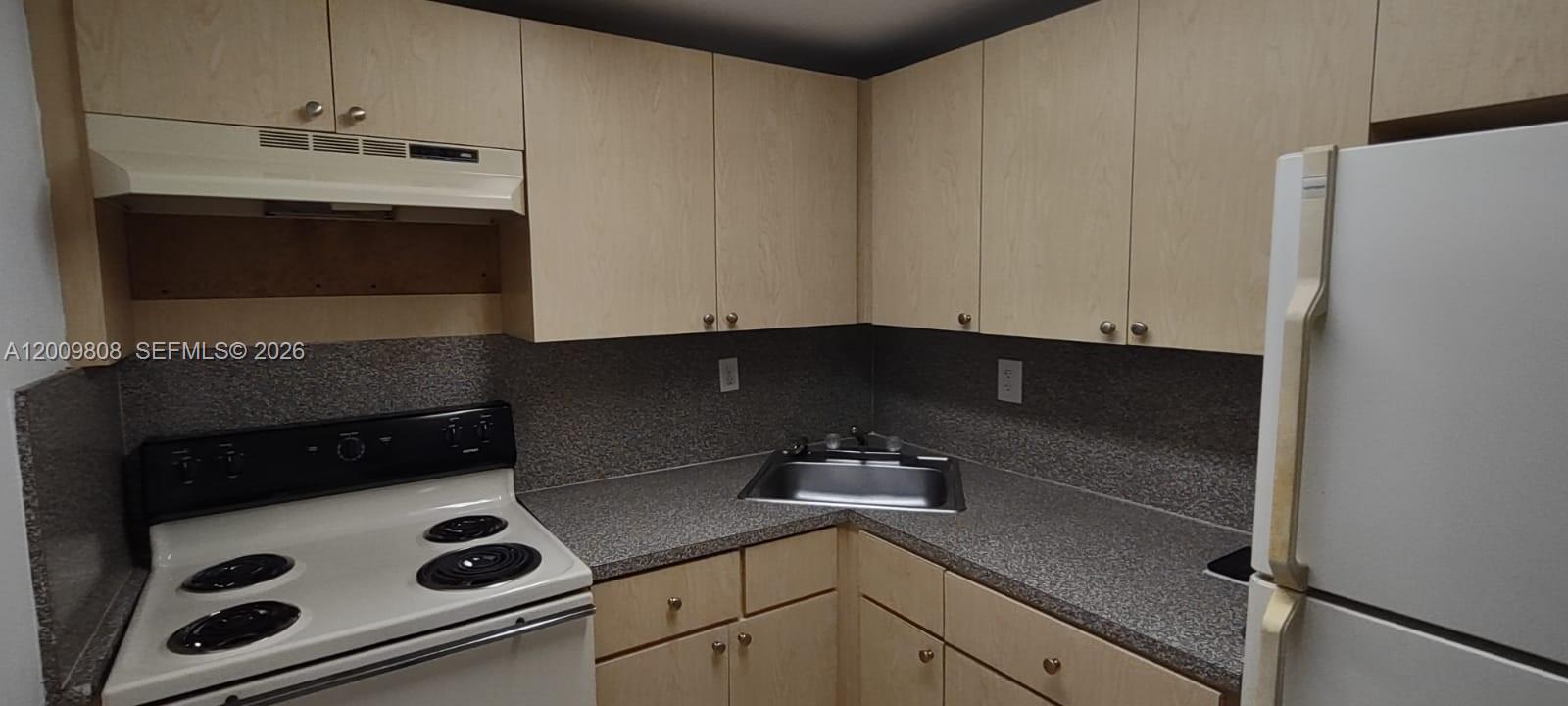 A kitchen features light wood cabinets, a white stove, a corner sink, and speckled countertops — 606 W 81st St # 309, Hialeah FL 33014, HIALEAH, FL