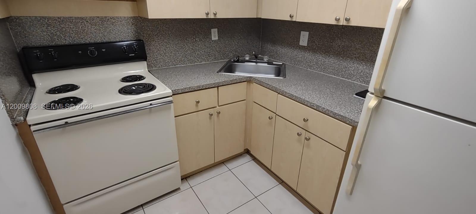 A small kitchen features light wood cabinets, a corner sink, and white appliances — 606 W 81st St # 309, Hialeah FL 33014, HIALEAH, FL