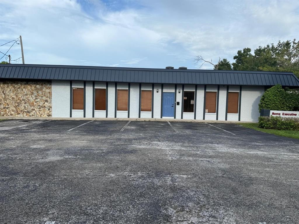 A single-story commercial building with a stone facade, dark metal roof, and blue front door — 13506 N ROME AVENUE, TAMPA, FL
