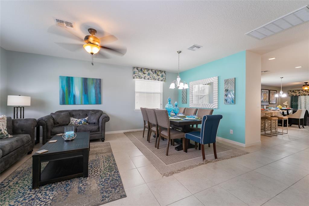 An open-concept living and dining area features light blue walls, tile flooring, and neutral furniture — 1355 YORKSHIRE COURT, DAVENPORT, FL